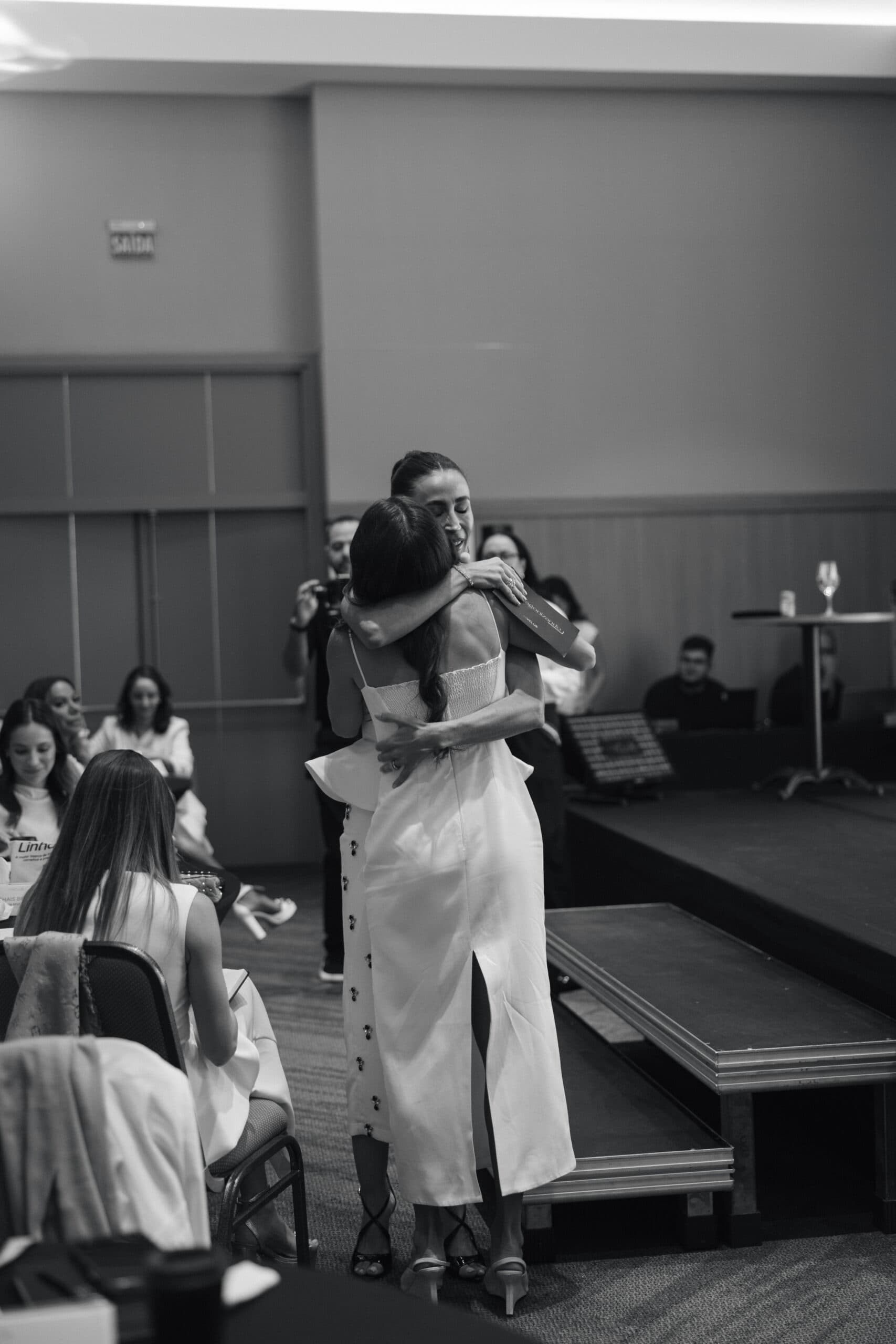 Marília abraça uma mulher durante um encontro, diante da plateia.